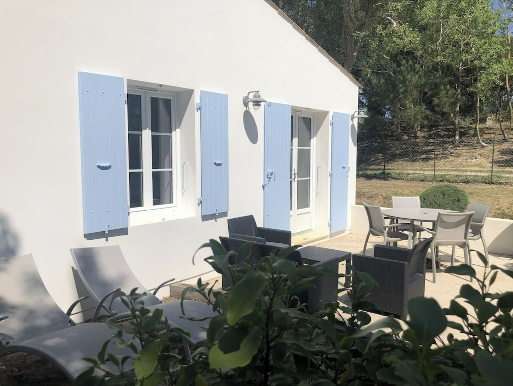 Un bâtiment blanc avec des volets bleus, des tables et chaises à l’extérieur et des plantes en pot.