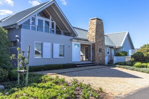 A modern two-story house with a stone chimney, large windows, and a well-maintained garden.