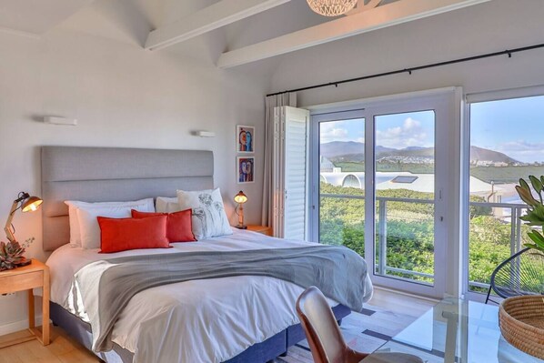 A modern bedroom with a large bed, a nightstand, a lamp, and a view of the outdoors.