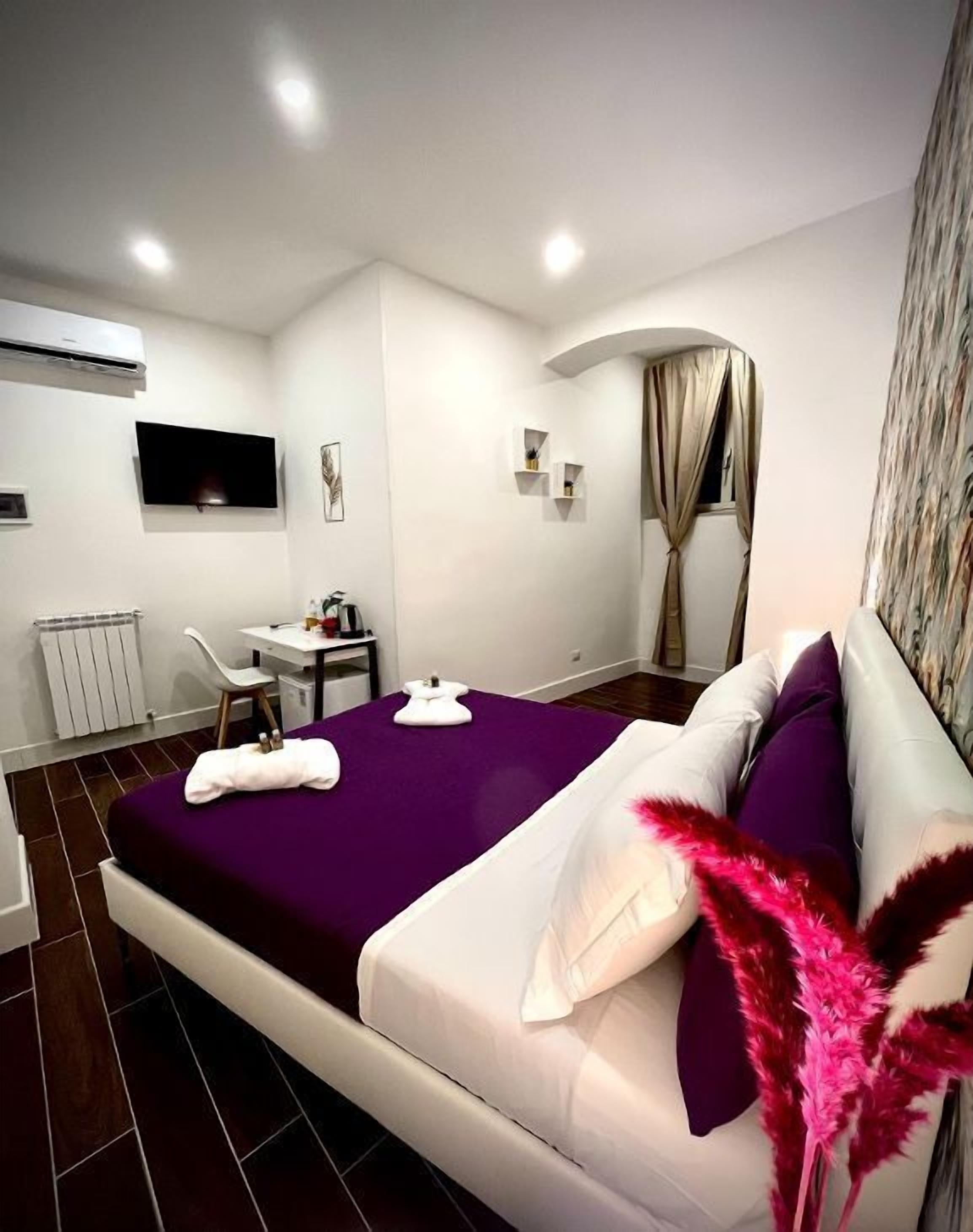 Une chambre d’hôtel moderne dotée d’un grand lit, d’un bureau, d’une chaise, d’un téléviseur à écran plat et d’une fenêtre avec des rideaux.