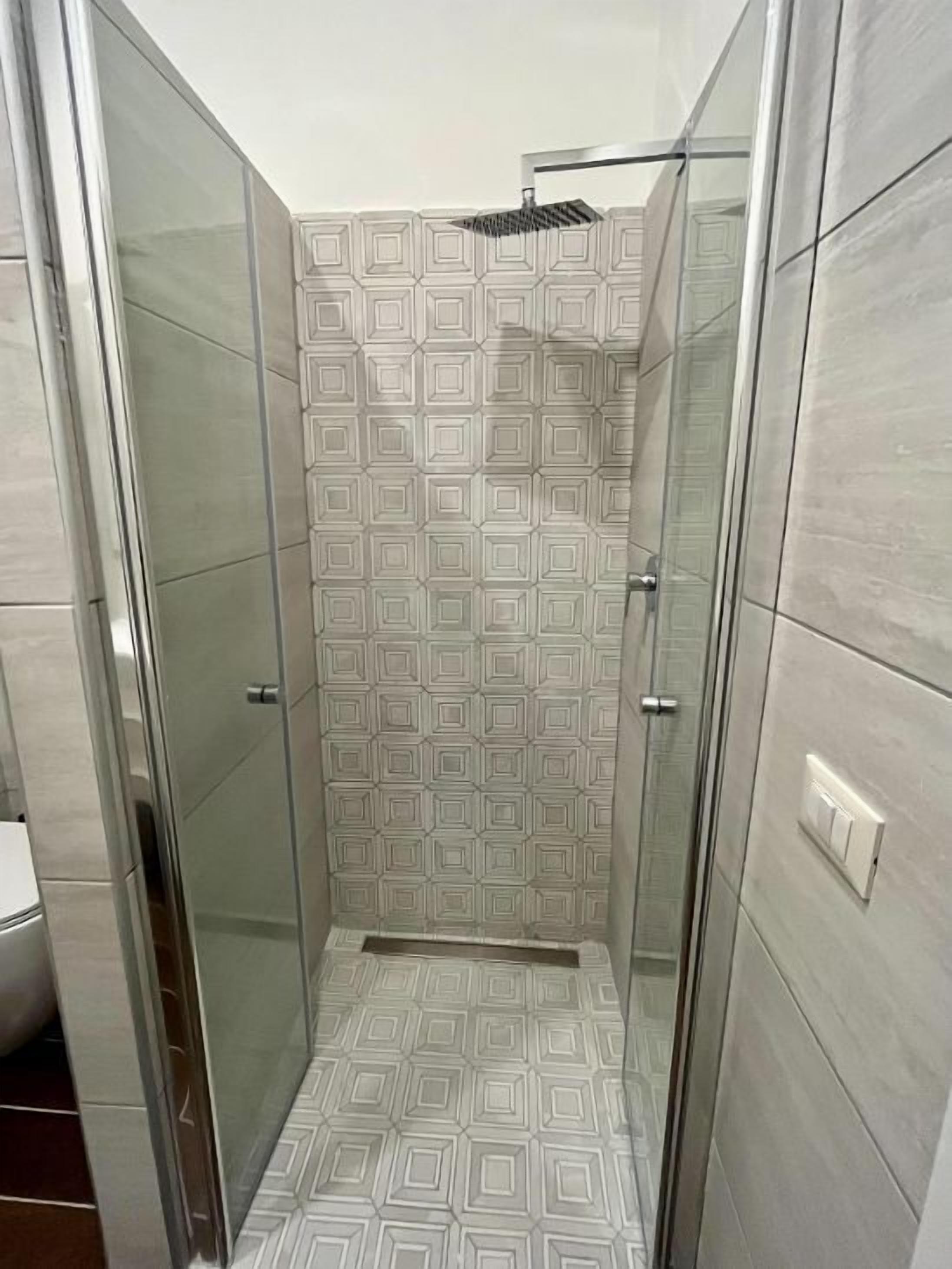 A shower with a geometric tile pattern, a glass door, and a light switch on the wall.