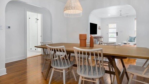 Een eetgedeelte met een houten tafel en witte stoelen, een witte deur en een hanglamp.