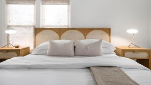 Een opgemaakt bed met witte lakens en twee kussens, aan weerszijden geflankeerd door twee nachtkastjes met lampen.