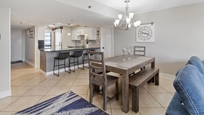 A modern kitchen with a central island, bar stools, and a dining table with chairs. - Mainsail 332 - Updated Beachfront Condo, Free Bch Svc, Pool, Hot Tub, Tennis! (Miramar Beach)
