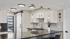 A modern kitchen with a central island, pendant lights, and white cabinetry. - Mainsail 332 - Updated Beachfront Condo, Free Bch Svc, Pool, Hot Tub, Tennis! (Miramar Beach)