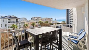 A balcony with a table and chairs, overlooking a beach and residential buildings. - Mainsail 332 - Updated Beachfront Condo, Free Bch Svc, Pool, Hot Tub, Tennis! (Miramar Beach)