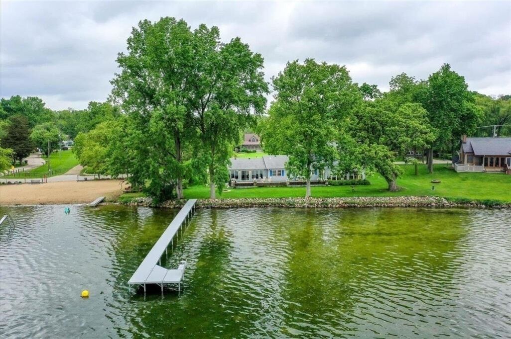 Une vue sur le lac, avec un quai, des arbres et une maison en arrière-plan.