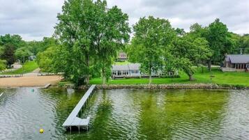 Une vue sur le lac, avec un quai, des arbres et une maison en arrière-plan.