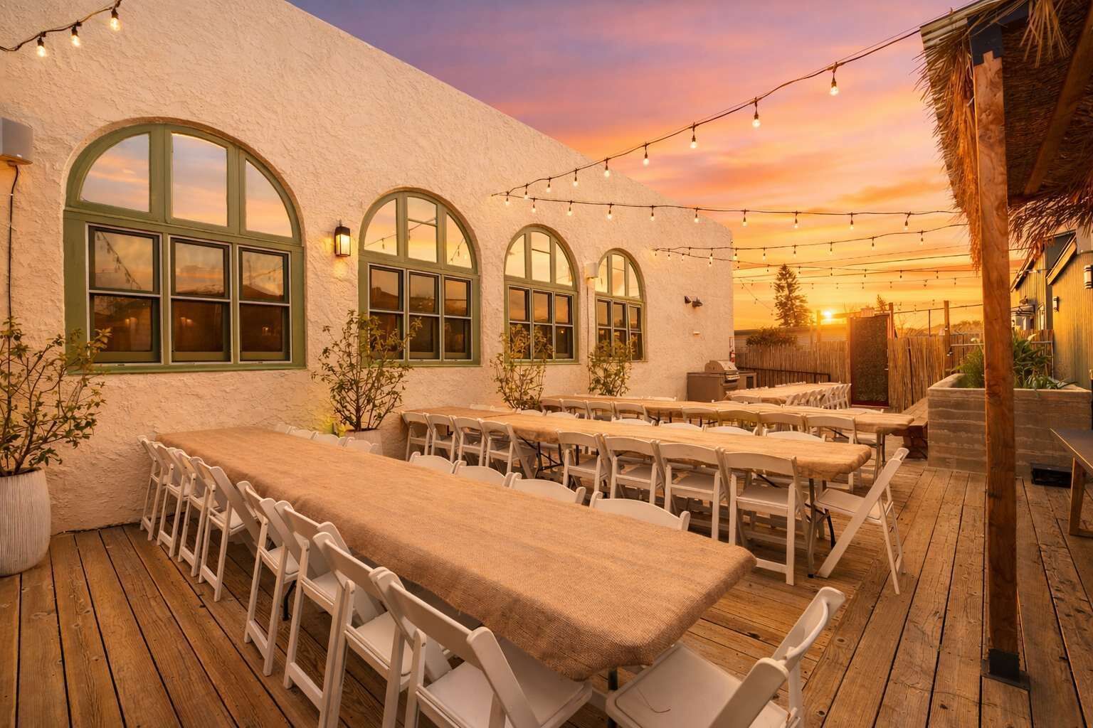 Una terraza con varias mesas y sillas, luces colgantes y vistas al atardecer.