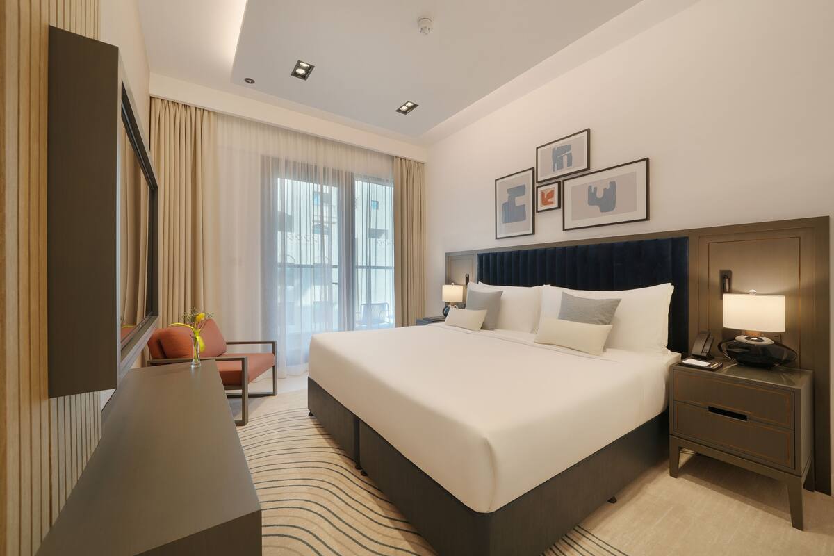 Une chambre d’hôtel avec un grand lit, un bureau, une chaise, une table de chevet et une fenêtre avec des rideaux.
