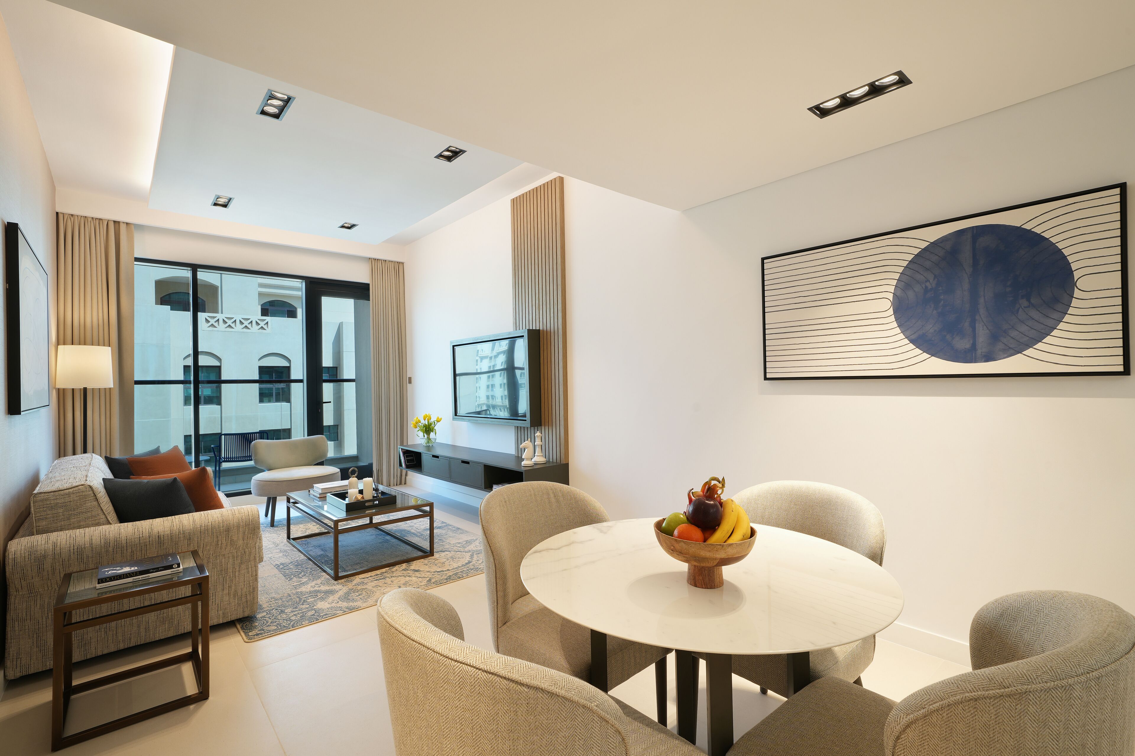 Uma sala de estar moderna com sofá, poltronas, mesa de centro e mesa de jantar com frutas.