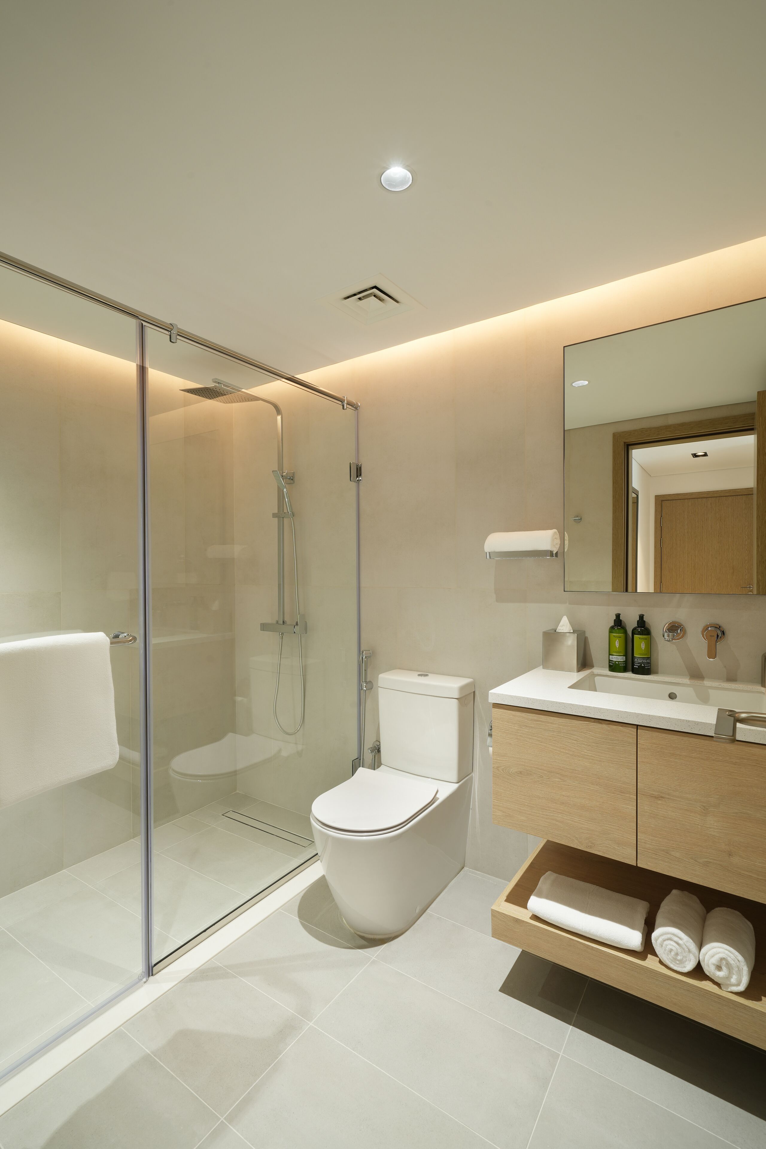 Un baño moderno con ducha envuelta en vidrio, inodoro blanco y tocador de madera con espejo.