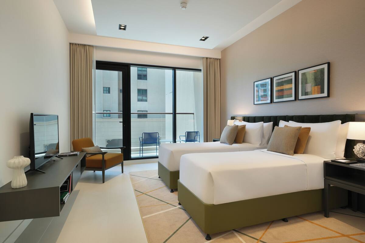 Une chambre d’hôtel avec deux lits, un bureau, une chaise, une télévision et un balcon donnant sur la ville.