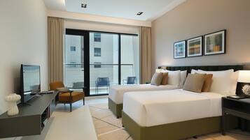 A hotel room with two beds, a desk, a chair, a TV, and a balcony with a view of the city.
