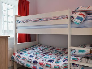 A bunk bed with a patterned bedspread and pillows, a window with red curtains, and a wooden dresser. - 2 bedroom accommodation in Keswick (Keswick)