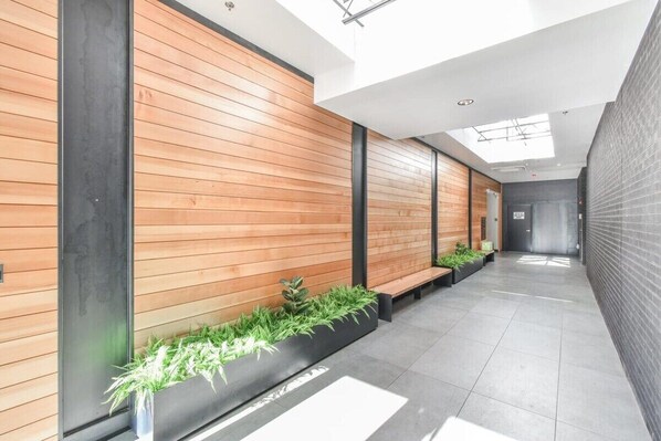Un pasillo moderno con paneles de madera, bancos negros y macetas con plantas verdes.