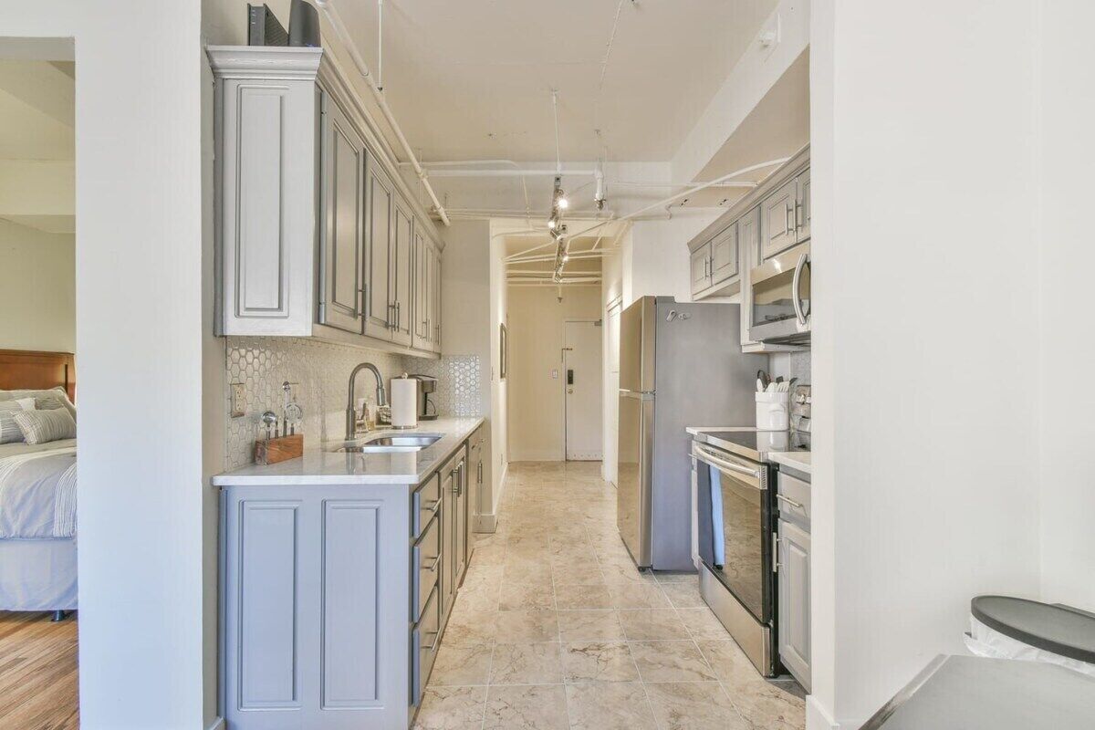 A narrow kitchen with white cabinetry, a central island, and a refrigerator.