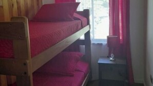 Ein Etagenbett mit roter Matratze in einem Zimmer, das einen kleinen Tisch und eine Lampe beinhaltet.