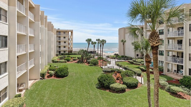 A hotel courtyard with a pool, palm trees, and a view of the ocean. - 🌴Ocean View Condo on No-Drive Beach-Castle Reef 312🌴 (New Smyrna Beach)