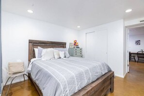Ein Schlafzimmer mit einem hölzernen Kopfende, einem Bett mit grauer Musterdecke, einem Nachttisch mit Lampe und einer kleinen Kommode.