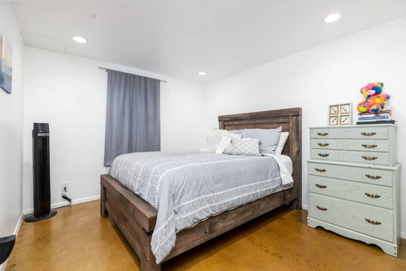 Una camera da letto con un letto di legno, una cassettiera bianca e una tenda grigia.