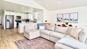 A modern living room with a sectional sofa, a kitchen in the background, and a dining area with chairs. - Hot Tub, Breakfast, and ideally located near Olympic National Park (Forks)