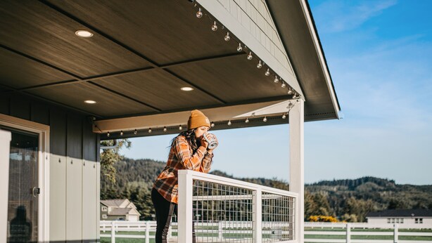 A person standing on a wooden deck with a railing, overlooking a rural landscape with houses and hills. - Hot Tub, Breakfast, and ideally located near Olympic National Park (Forks)