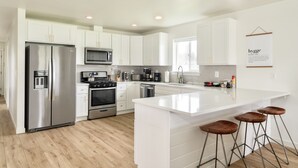 A modern kitchen with white cabinetry, stainless steel appliances, and a central island with stools. - Hot Tub, Breakfast, and ideally located near Olympic National Park (Forks)