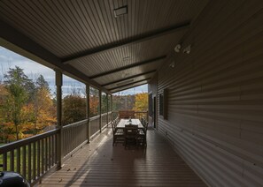 A covered porch with a wooden deck, a table, and chairs.