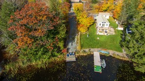 A house with a dock and a small boat, surrounded by autumn-colored trees. - Babcock Lake Luxury Retreat: Direct Waterfront, Deck & Huge Game Room (Petersburgh)