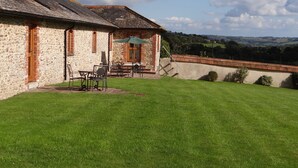 Une construction en pierre avec une cheminée en briques, une terrasse dotée de mobilier d’extérieur et une vue sur la campagne.