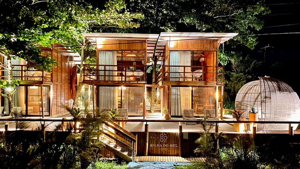 A two-story wooden building with a glass facade, outdoor seating, and a dome structure. - Ilha do Mel Lodges (Paranaguá)