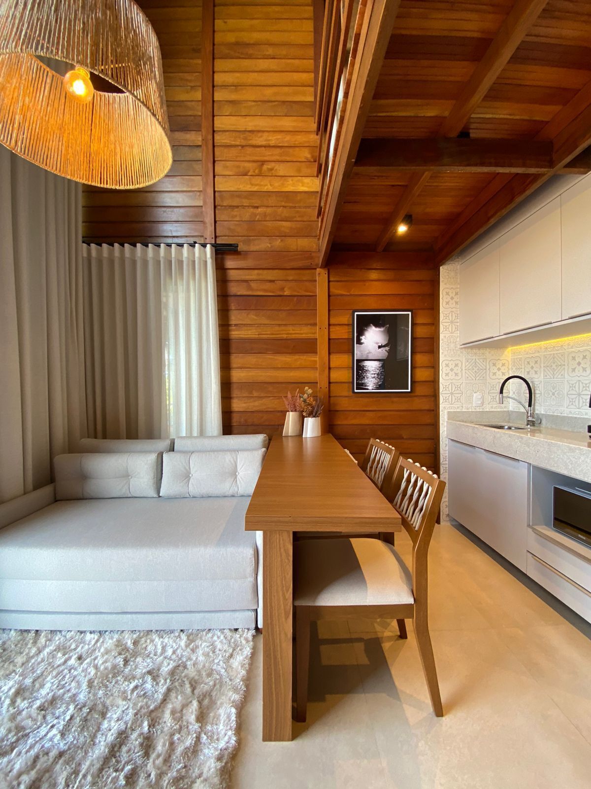 Una sala de estar moderna con techo de madera, un sofá, una mesa de comedor y una zona de cocina.