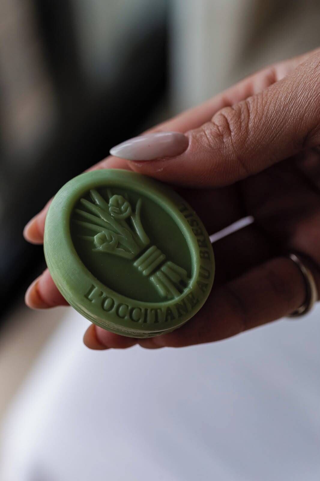 A hand holding a green wax seal with embossed text.