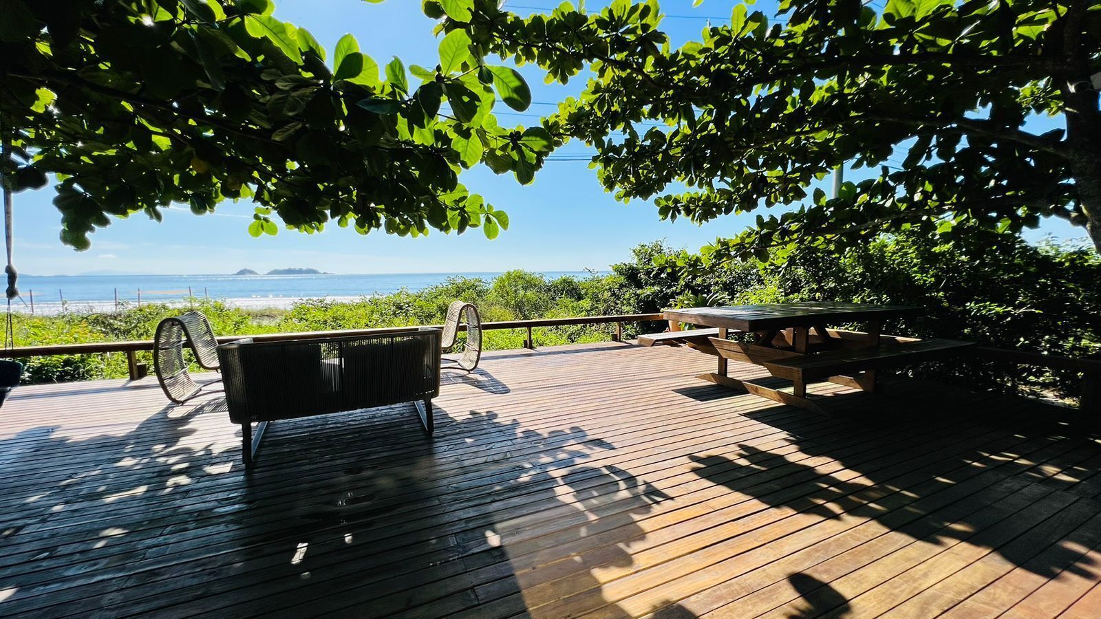 Una terraza de madera con un banco y una mesa de picnic, con vista a una playa y el océano.