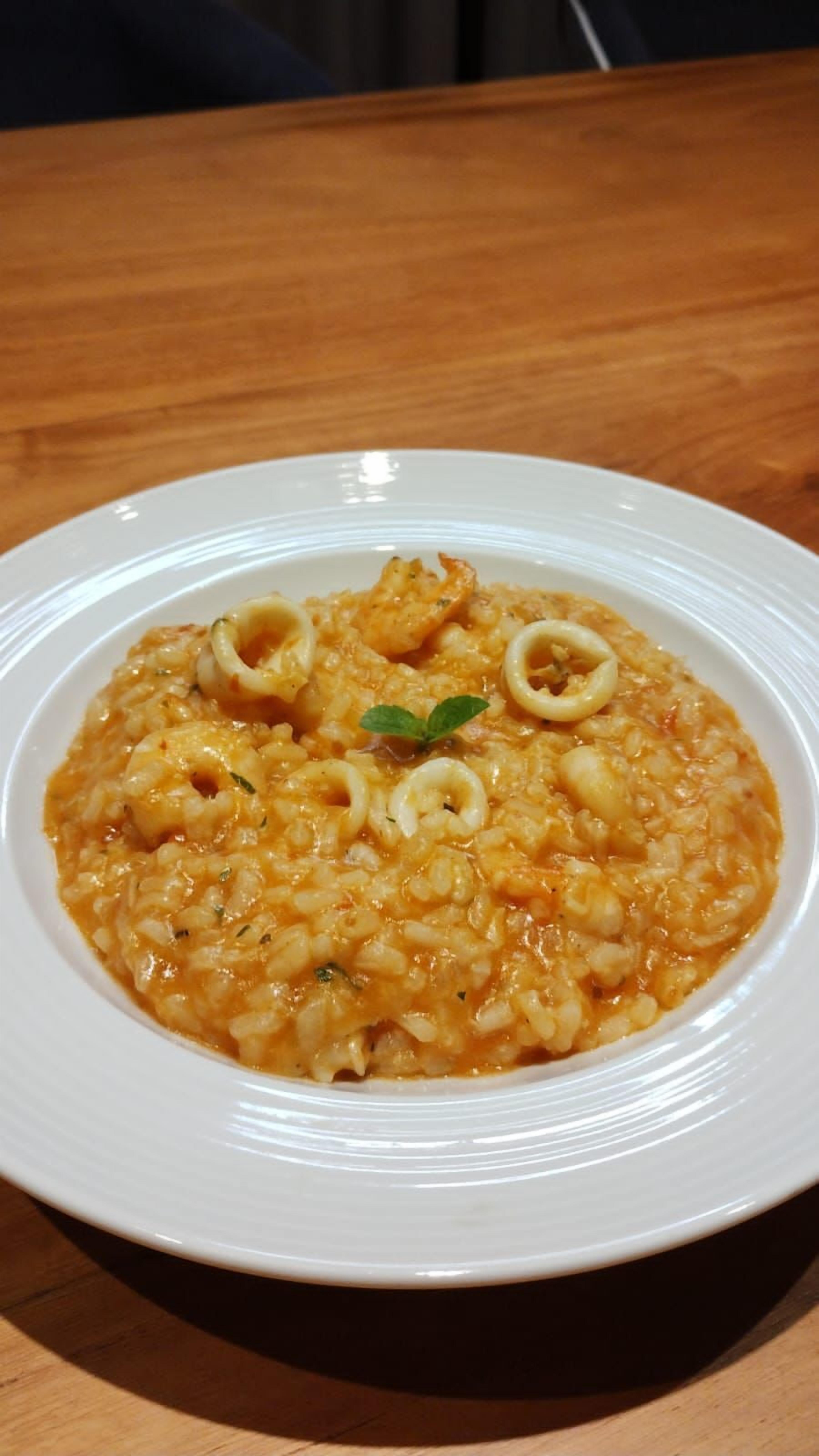 Un plato de risotto de mariscos con aros de calamares y una ramita de hierbas sobre un plato blanco.