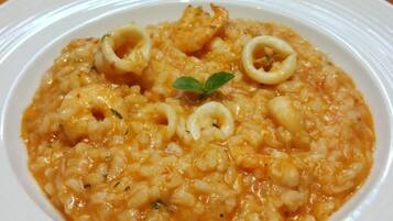 Un plato de risotto de mariscos con aros de calamares y una ramita de hierbas sobre un plato blanco.