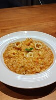 Un plato de risotto de mariscos con aros de calamares y una ramita de hierbas sobre un plato blanco.