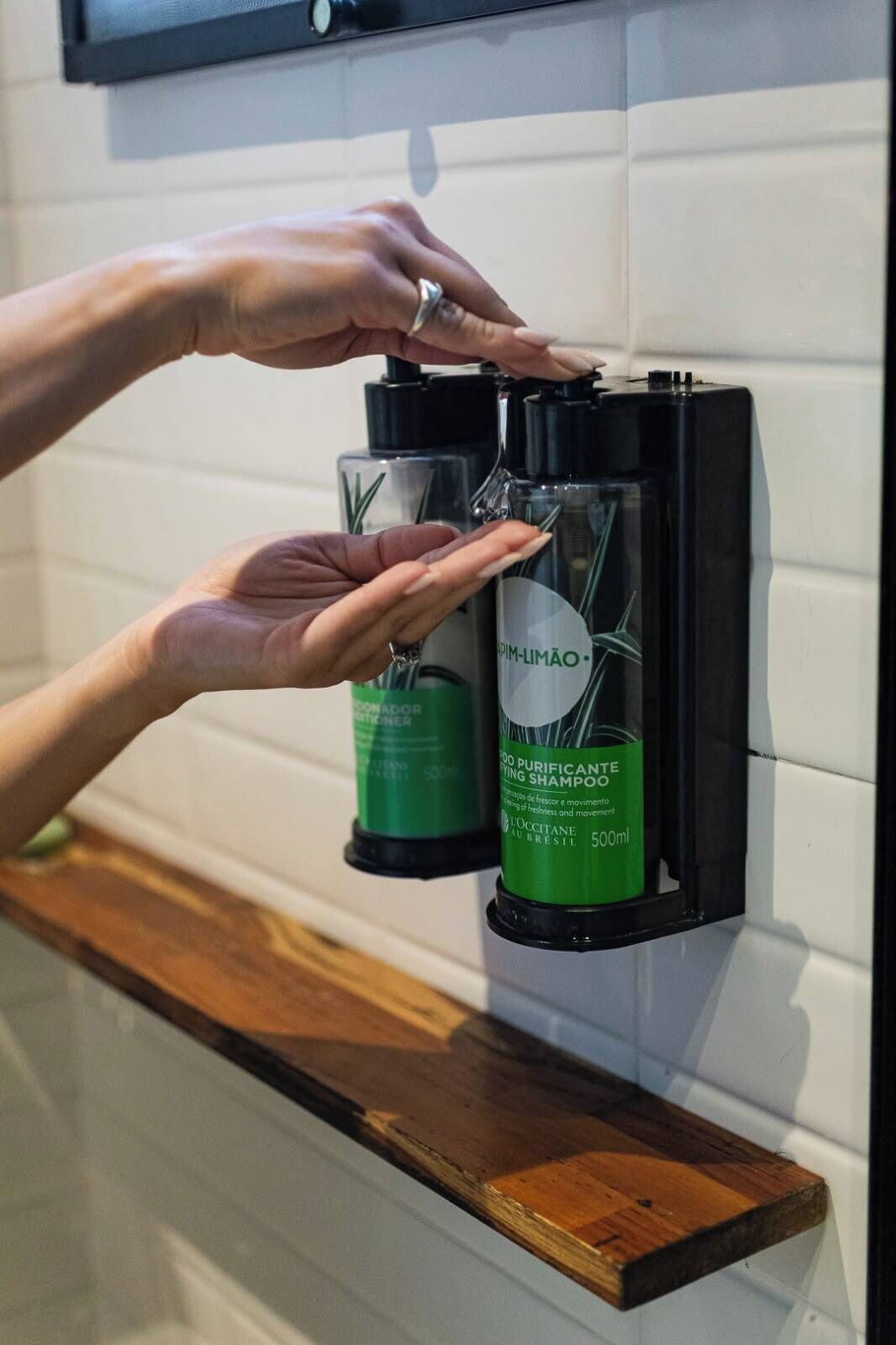 A person dispensing shampoo from a dispenser on a shelf.