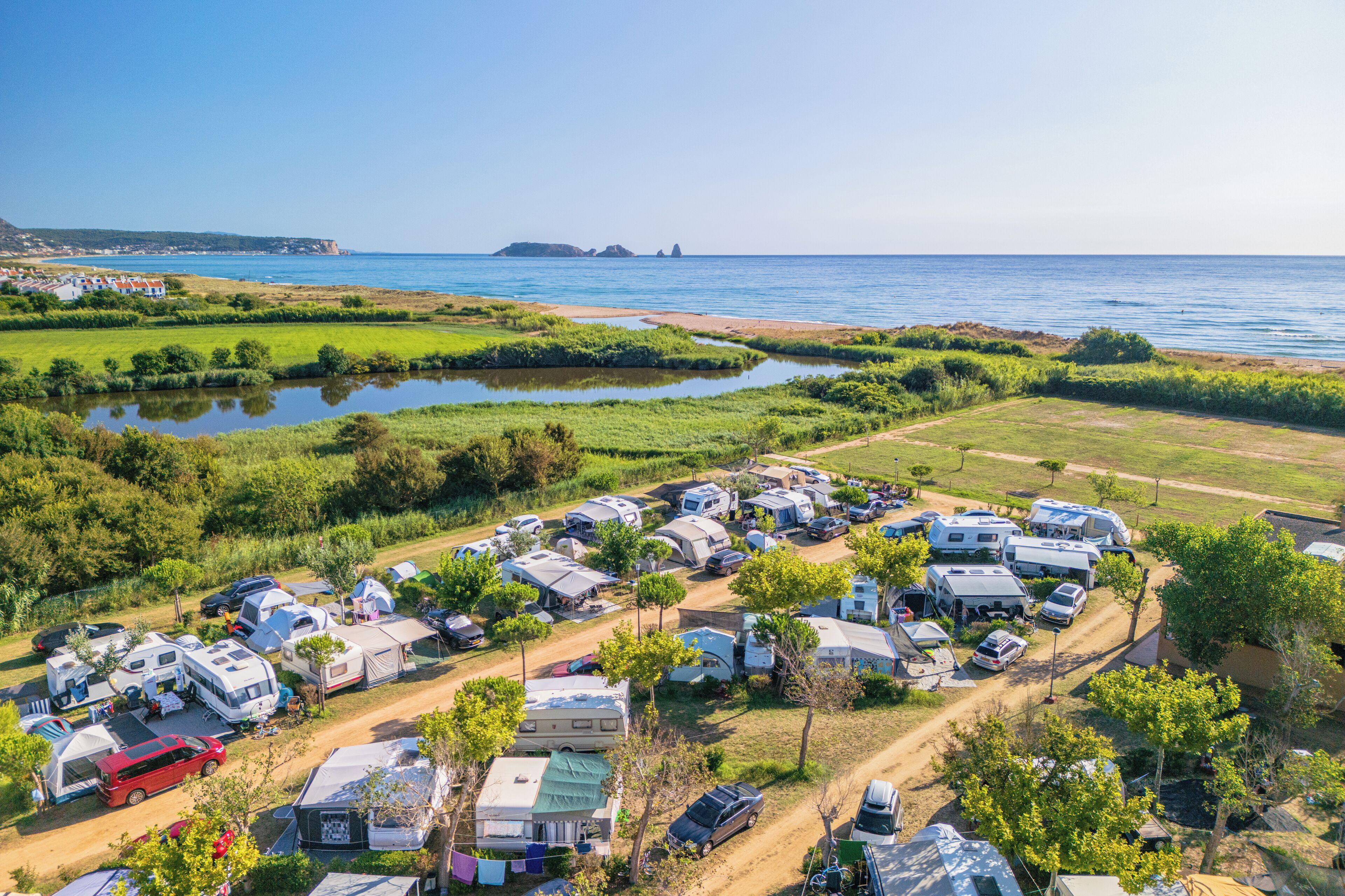 Un camping con vehículos recreativos y tiendas de campaña, un sendero de tierra y una masa de agua.