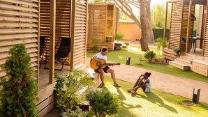 Una terraza de madera con una persona tocando la guitarra, una zona de estar cubierta y un césped bien cuidado.