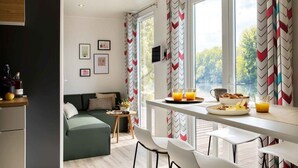Una cocina moderna con comedor, ventanas amplias con cortinas estampadas, un sofá verde y una mesa pequeña con cosas para el desayuno.