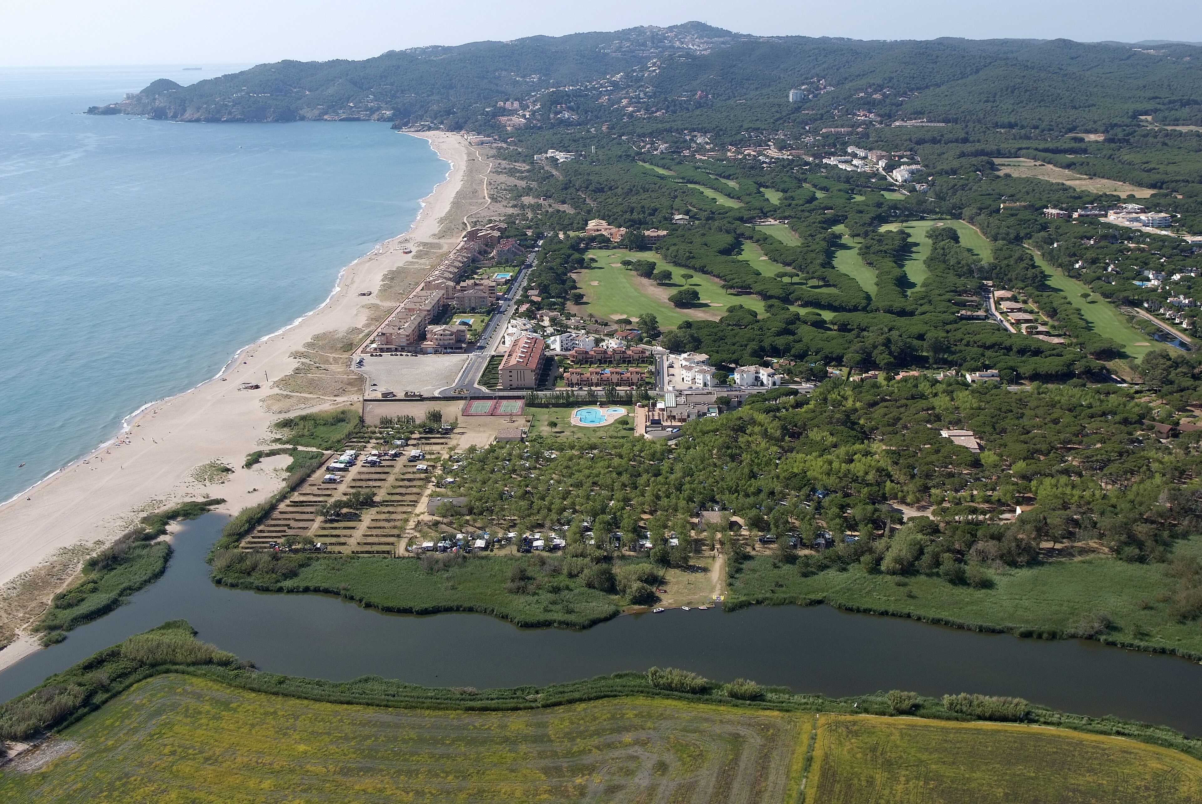 An aerial view of a coastal area with a beach, golf course, and residential buildings.