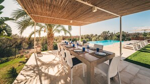 Een terras met eettafel gedekt voor zes personen, met uitzicht op een zwembad en weelderige begroeiing.
