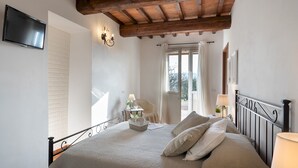 A bedroom with a bed, a TV mounted on the wall, a window with curtains, and a wooden ceiling. - Casa La Fenice 8+2, Emma Villas (Pomarance)
