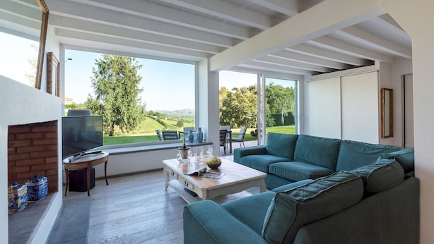 Uma sala de estar moderna com um sofá verde, uma televisão e uma lareira. Há uma janela grande que oferece vista para o exterior.