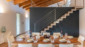 A dining area with a wooden table set for six, a modern staircase, and a large window providing natural light. - Villa Kimia 8, Emma Villas (Acireale)