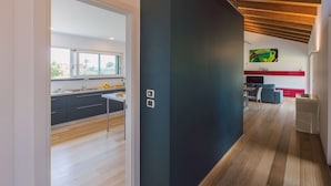 A modern kitchen with dark cabinets, a wooden floor, and a view of the city through large windows. - Villa Kimia 8, Emma Villas (Acireale)