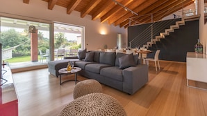 A modern living room with a grey sofa, a round coffee table, and a staircase leading to an upper level. - Villa Kimia 8, Emma Villas (Acireale)