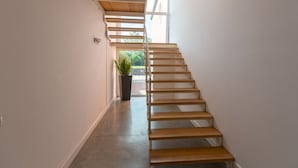 A modern staircase with wooden steps and metal railings, leading to a bright room with a large window and a potted plant. - Villa Kimia 8, Emma Villas (Acireale)